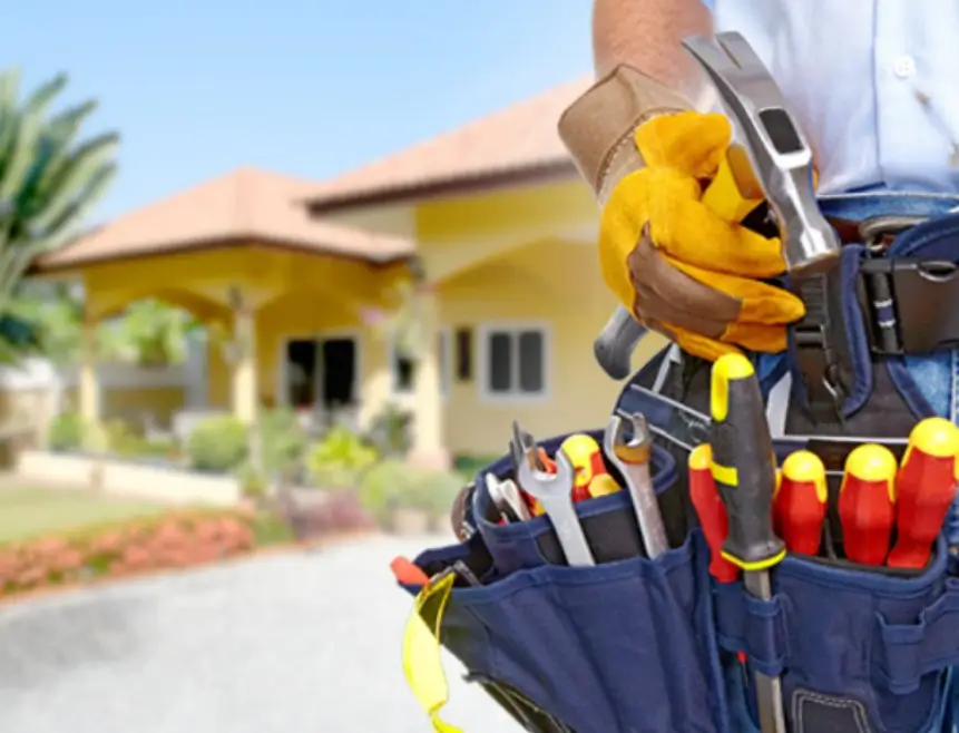 Tradesman’s tool belt filled with tools in front of a white picket house, representing property maintenance services